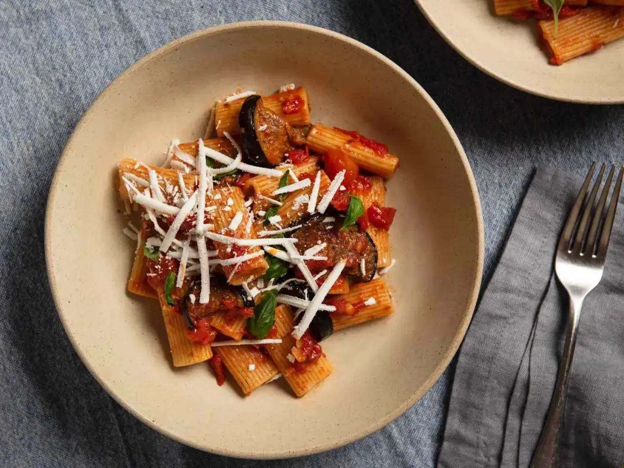 Pyszne danie pasta alla norma z makaronem rigatoni, bakłażanem, pomidorami i startym serem.