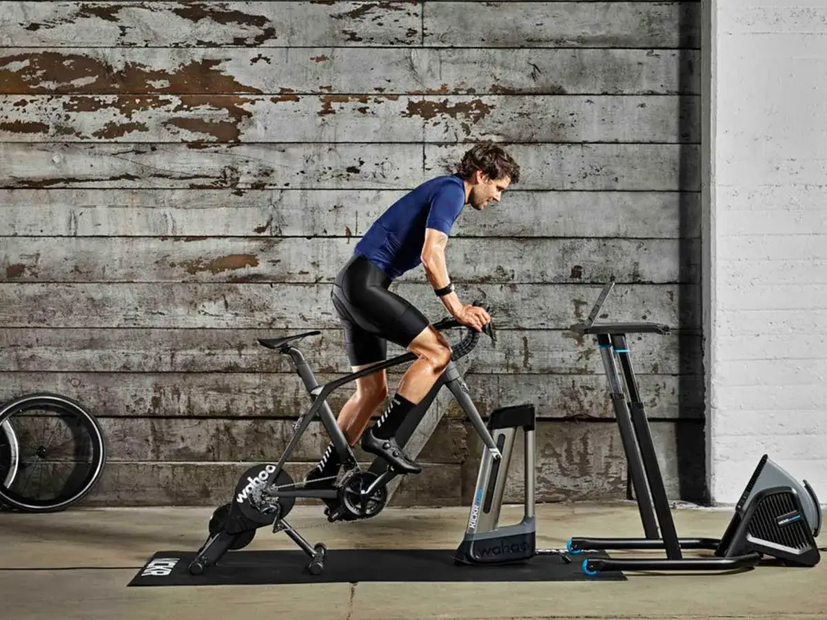 Man in cycling gear trains intensely in his cycling pain cave, a Wahoo Kickr trainer and laptop setup ready for a tough workout.