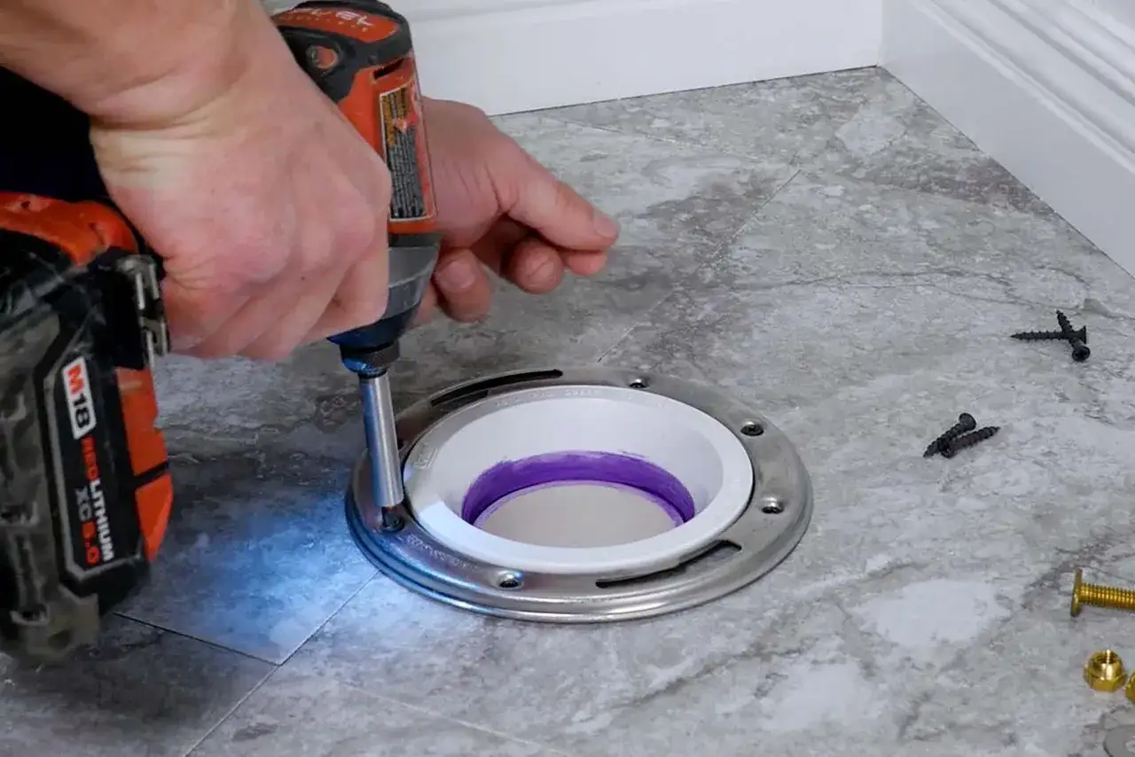 A person uses a drill to secure a new toilet flange, a key step in how to replace a toilet flange.