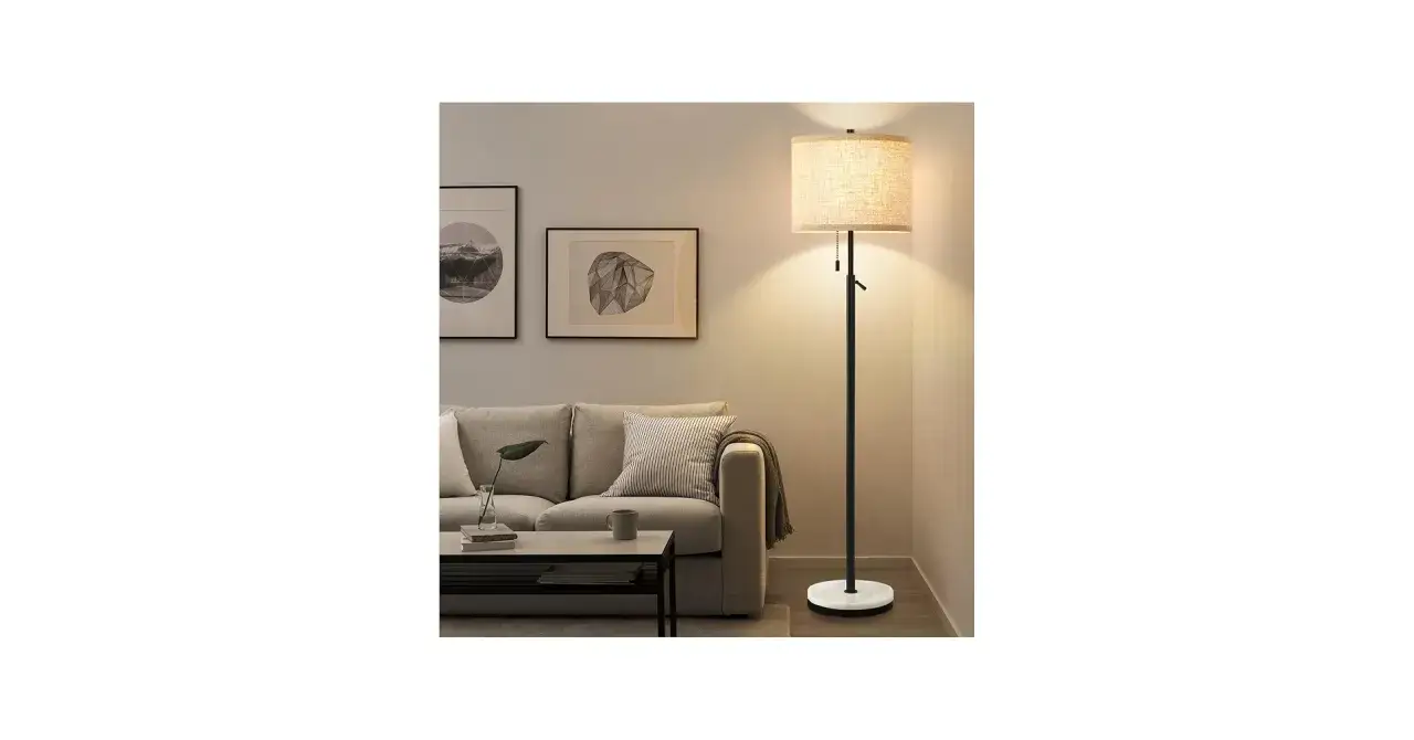 Una lámpara de suelo ilumina un rincón acogedor del salón, junto a un sofá gris y cuadros modernos.