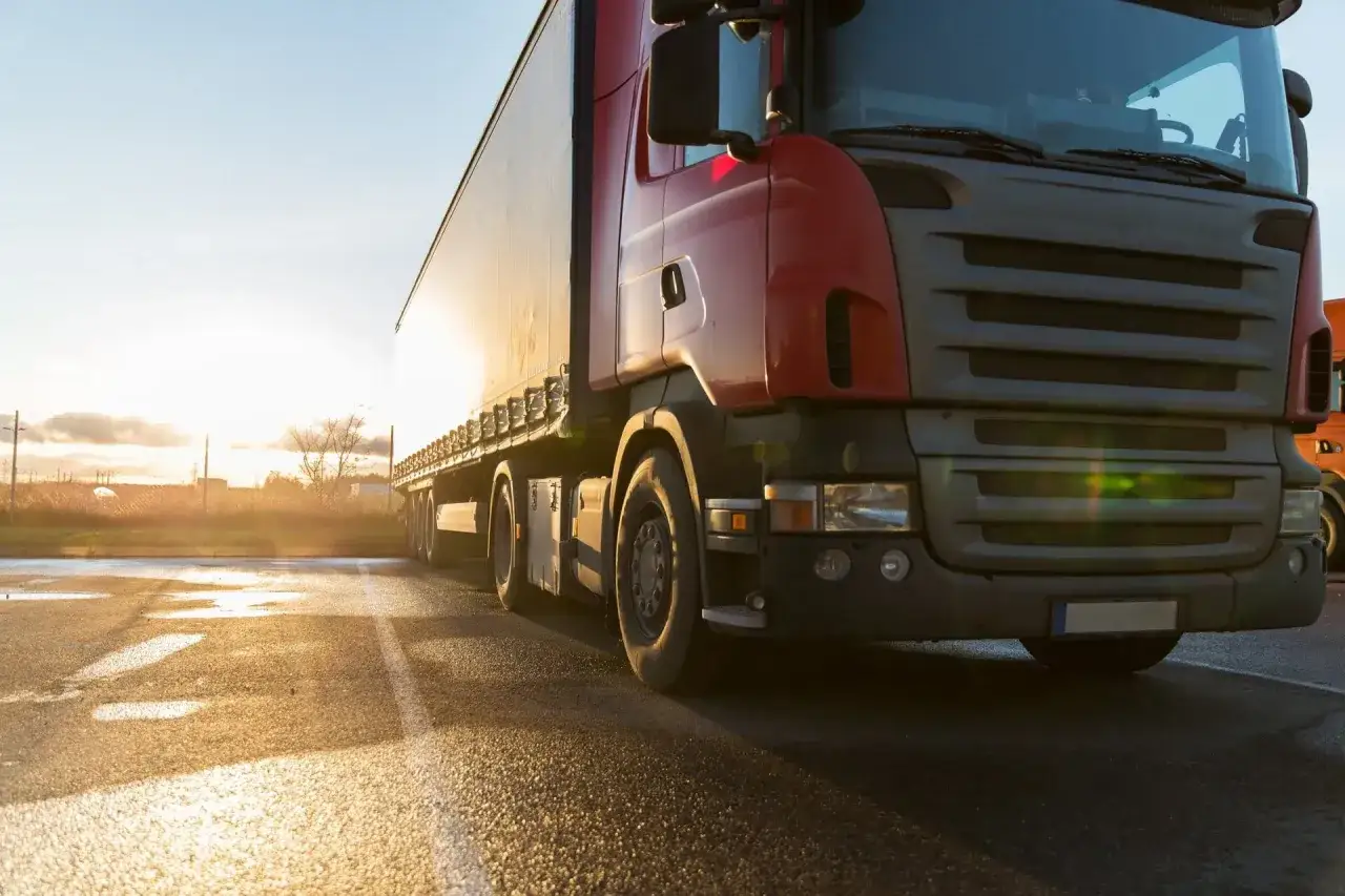Czerwona ciężarówka gotowa do transportu Hiszpania Polska. Słońce odbija się od mokrej nawierzchni.