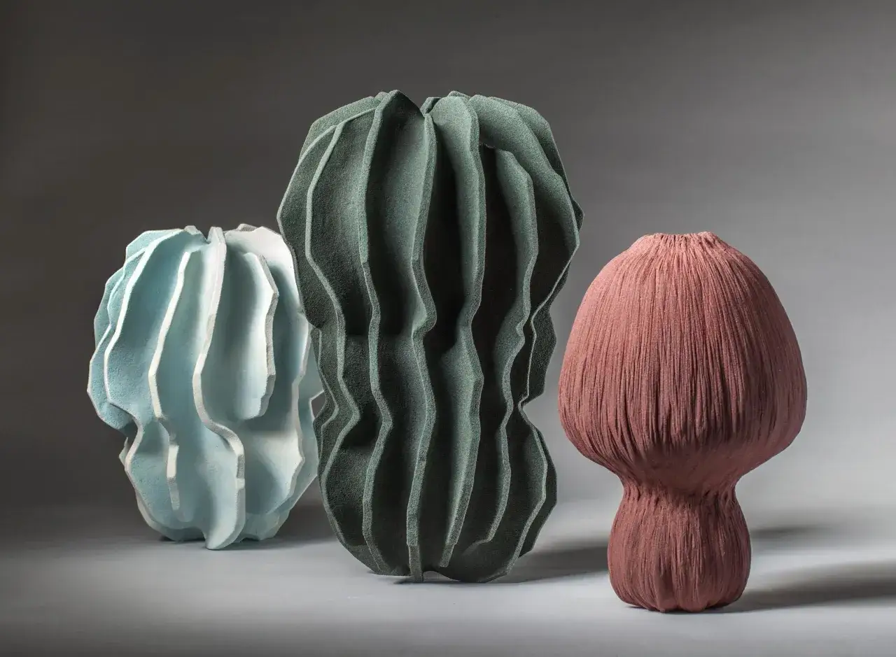 Three textured ceramic sculptures, exploring organic forms in art. A pale blue, a dark green, and a dusty rose piece stand against a grey background.