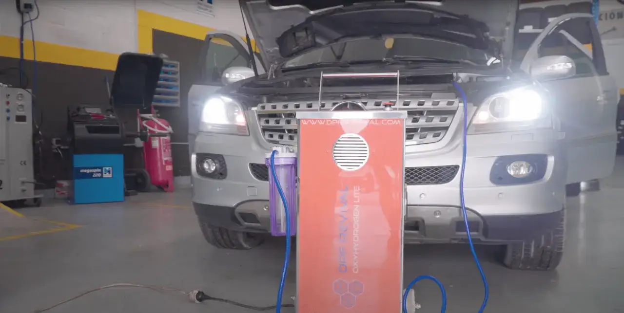 Un véhicule argenté est en cours de décalaminage hydrogène dans un atelier. Une machine orange est connectée au moteur.