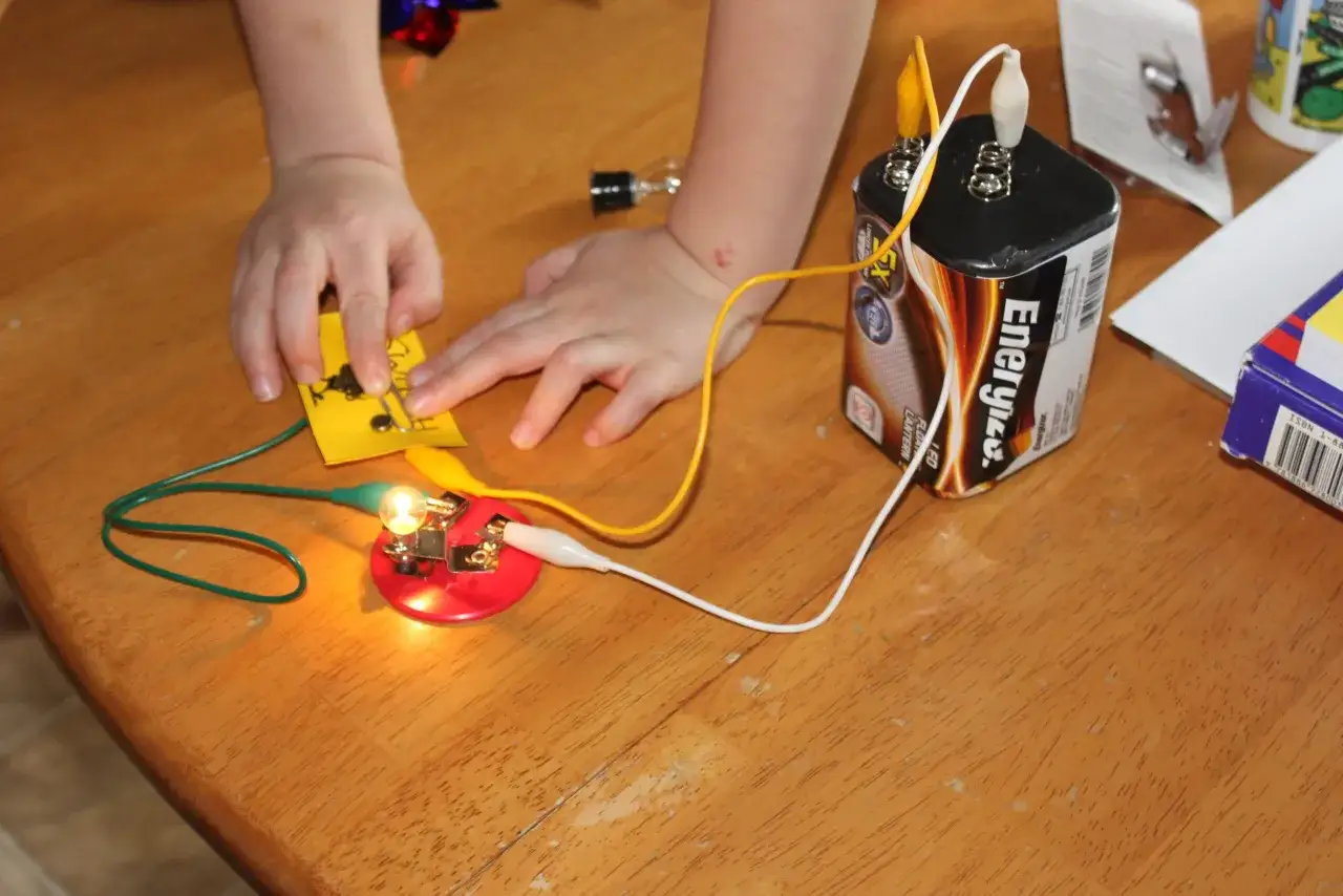 Kinder bauen einen Stromkreis. Eine Gl&uuml;hbirne leuchtet, w&auml;hrend sie mit einer Batterie verbunden ist. Ein spannendes Experiment f&uuml;r die Grundschule.