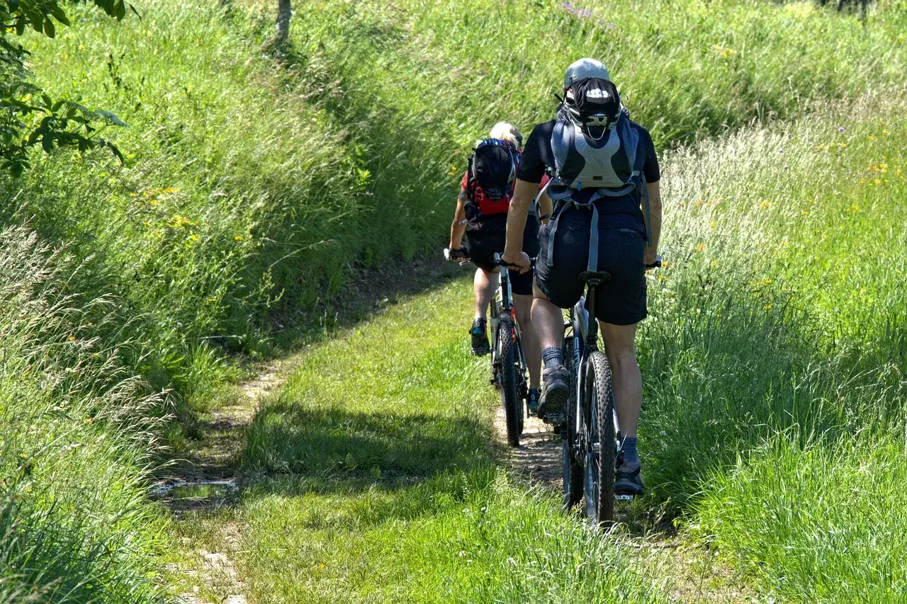 Tv&aring; personer cyklar p&aring; en grusv&auml;g kantad av h&ouml;gt gr&auml;s. En h&auml;rlig sommardag f&ouml;r cykeltur i &Aring;kersberga.