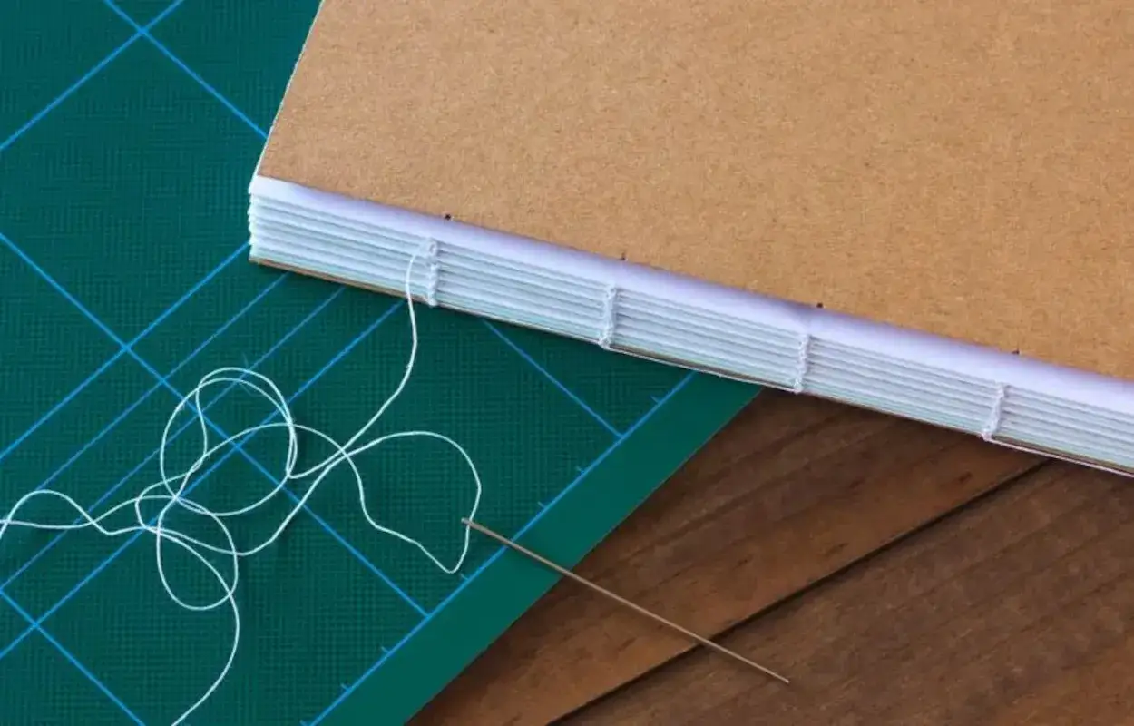 Dimostrazione di come rilegare fogli a mano con filo e ago, creando un quaderno artigianale.