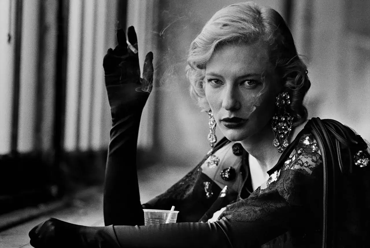 A woman with blonde hair and dramatic earrings, smoking a cigarette, in a style reminiscent of Peter Lindbergh's famous photos.