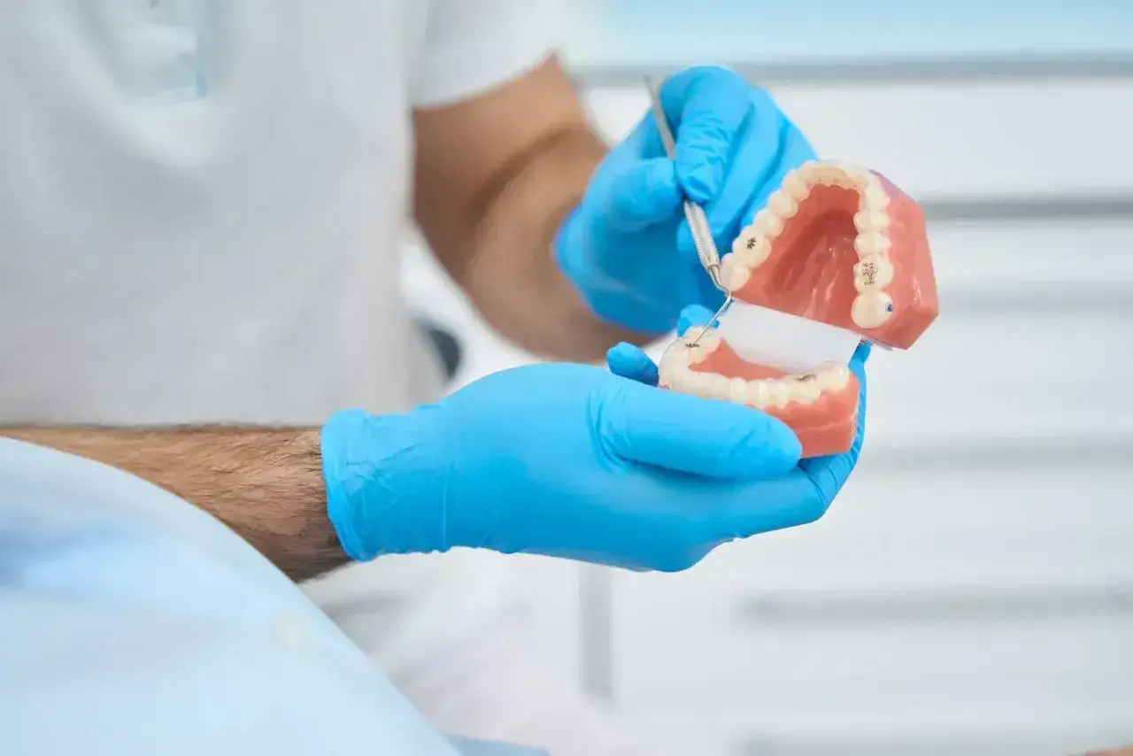 Dentysta w niebieskich rękawiczkach pokazuje model szczęki, wyjaśniając działanie protezy teleskopowej.
