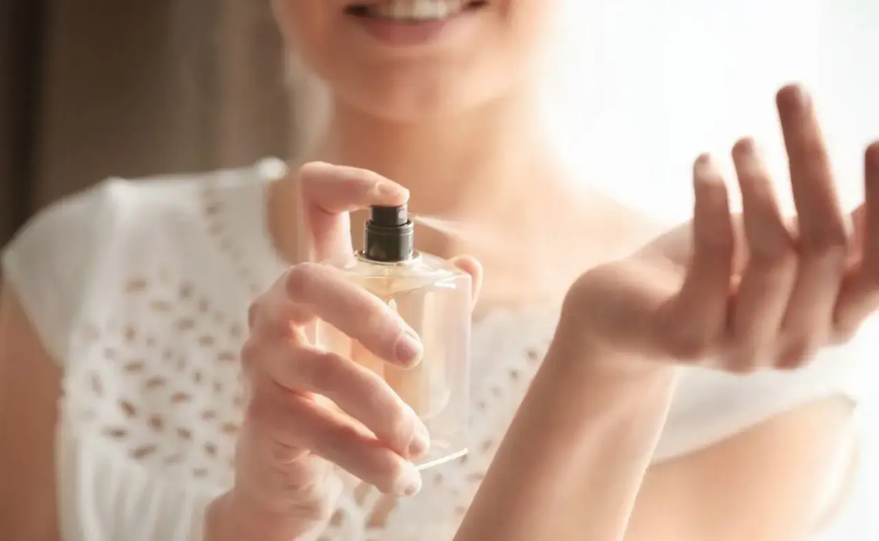 Kobieta rozpyla perfumy na nadgarstek, pokazując, jak używać perfum. Delikatny zapach otula skórę.