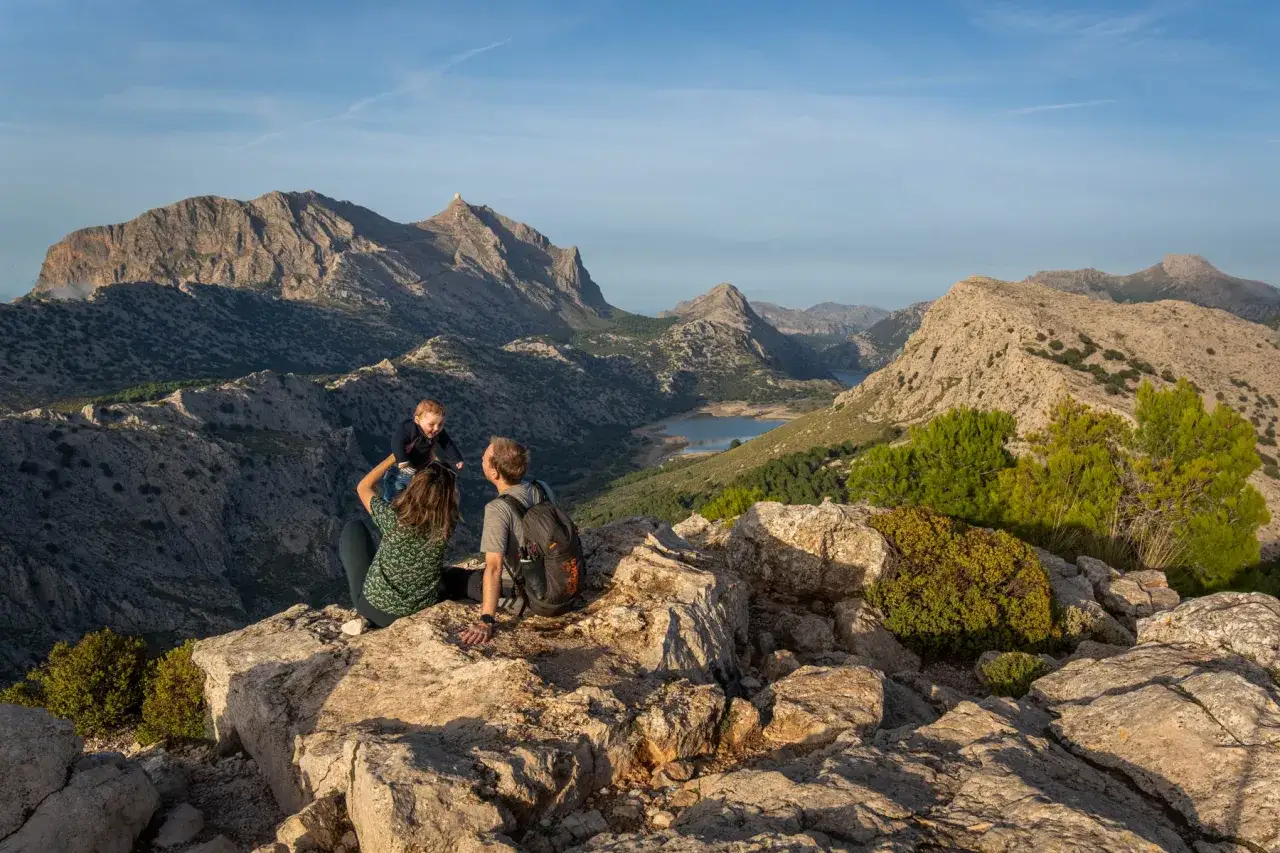 Familie genießt Aussicht auf einem Felsvorsprung, ein Kind wird hochgehoben. Im Hintergrund ein Stausee und Berge, typisch für einen fernwanderweg Mallorca.