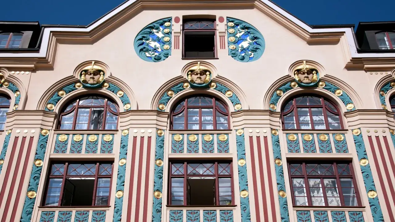 Fassade im Jugendstil mit Gesichtsmasken, geschwungenen Ornamenten und goldenen Akzenten.