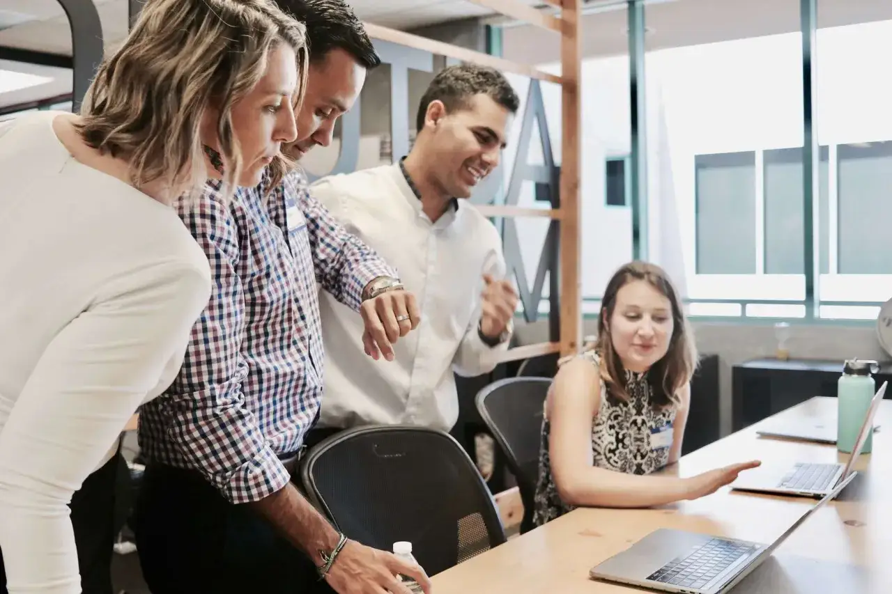 A staff supervisor and team collaborate around a laptop, discussing a project.