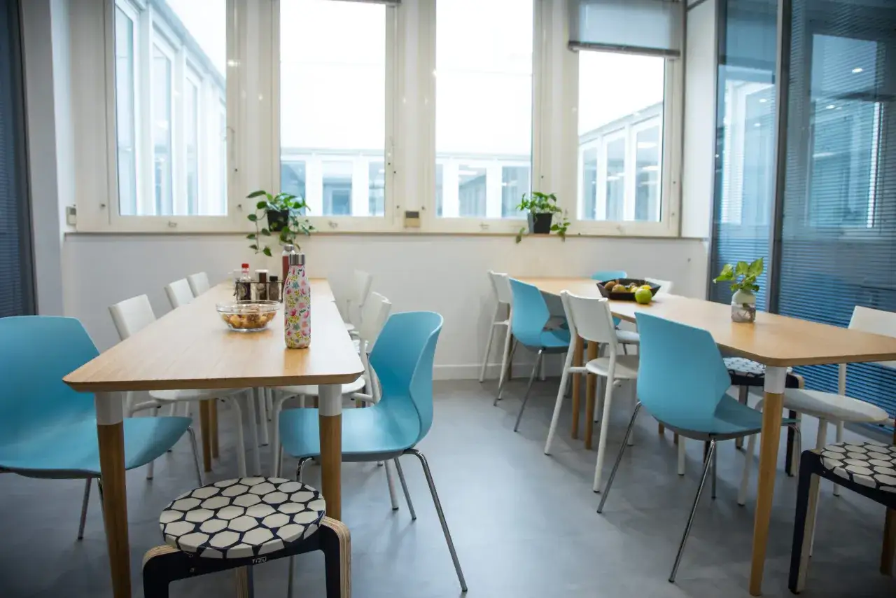 Salle à manger d'entreprise avec tables en bois, chaises bleues et blanches. Un repas d'entreprise obligatoire semble imminent.