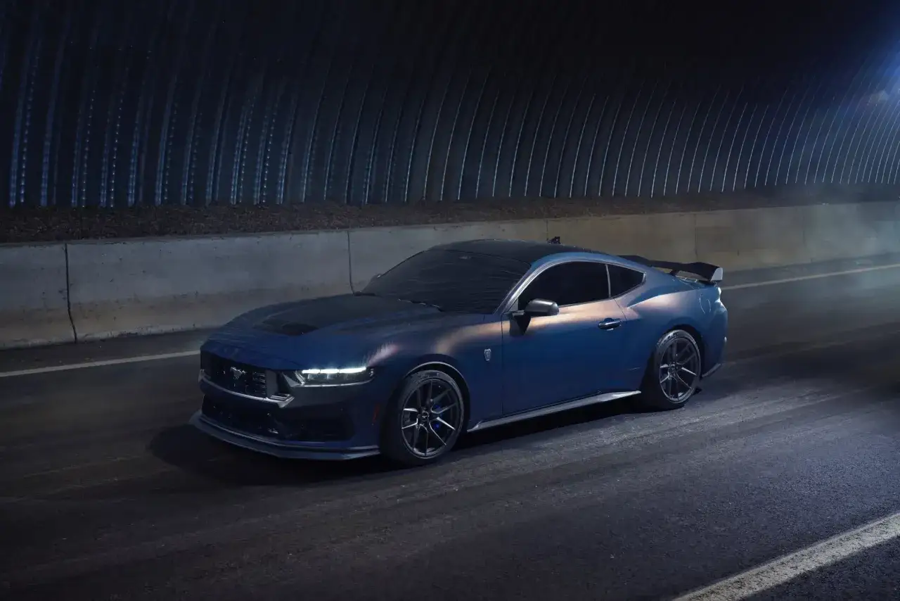 Niebieski Ford Mustang 2025 z czarnym dachem i spoilerem, gotowy do jazdy po nocnej trasie.