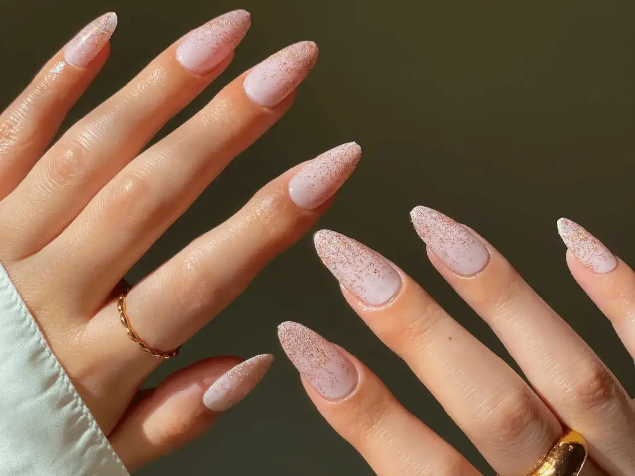 Mains d&eacute;licates aux ongles paillettes d&eacute;grad&eacute; rose p&acirc;le, orn&eacute;es de bagues fines.
