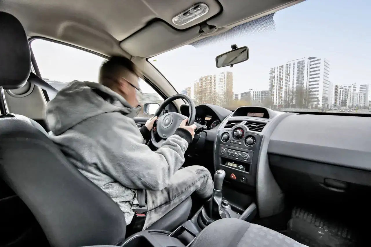Kierowca w szarej bluzie i jeansach prowadzi auto, które szarpie przy dodawaniu gazu. Benzyna może być przyczyną problemu.