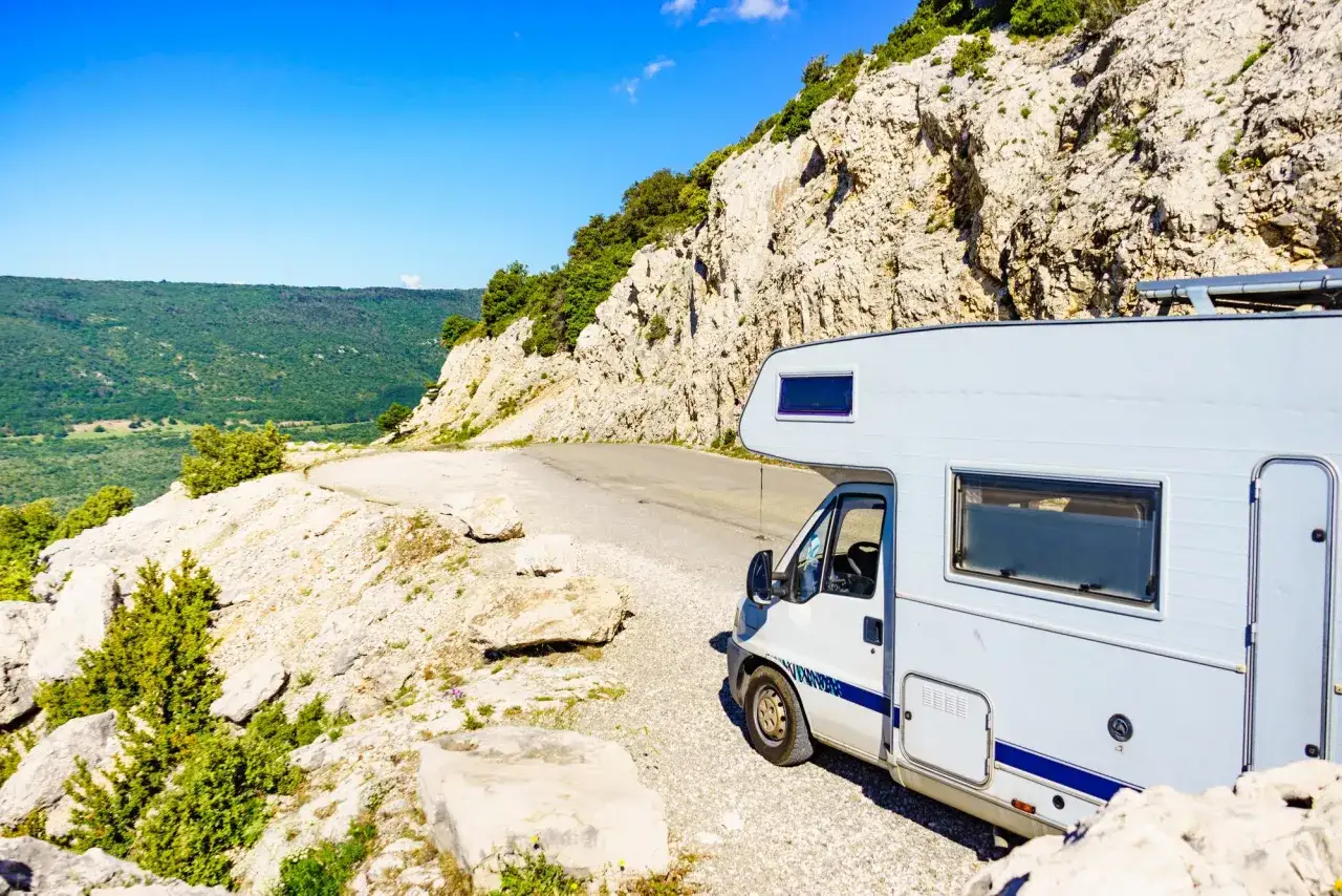 Un camping-car sauvage s'arrête sur une route de montagne rocailleuse, offrant une vue imprenable sur la vallée verdoyante.