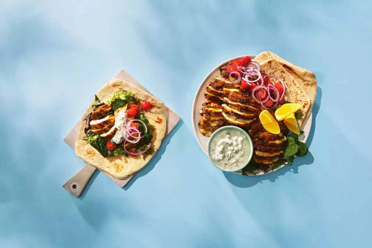 Zwei Portionen Chicken Tandoori: Ein Wrap mit Salat und eine Platte mit geschnittenem H&auml;hnchen, Tomaten, Zwiebeln, Zitronenspalten und Dip.