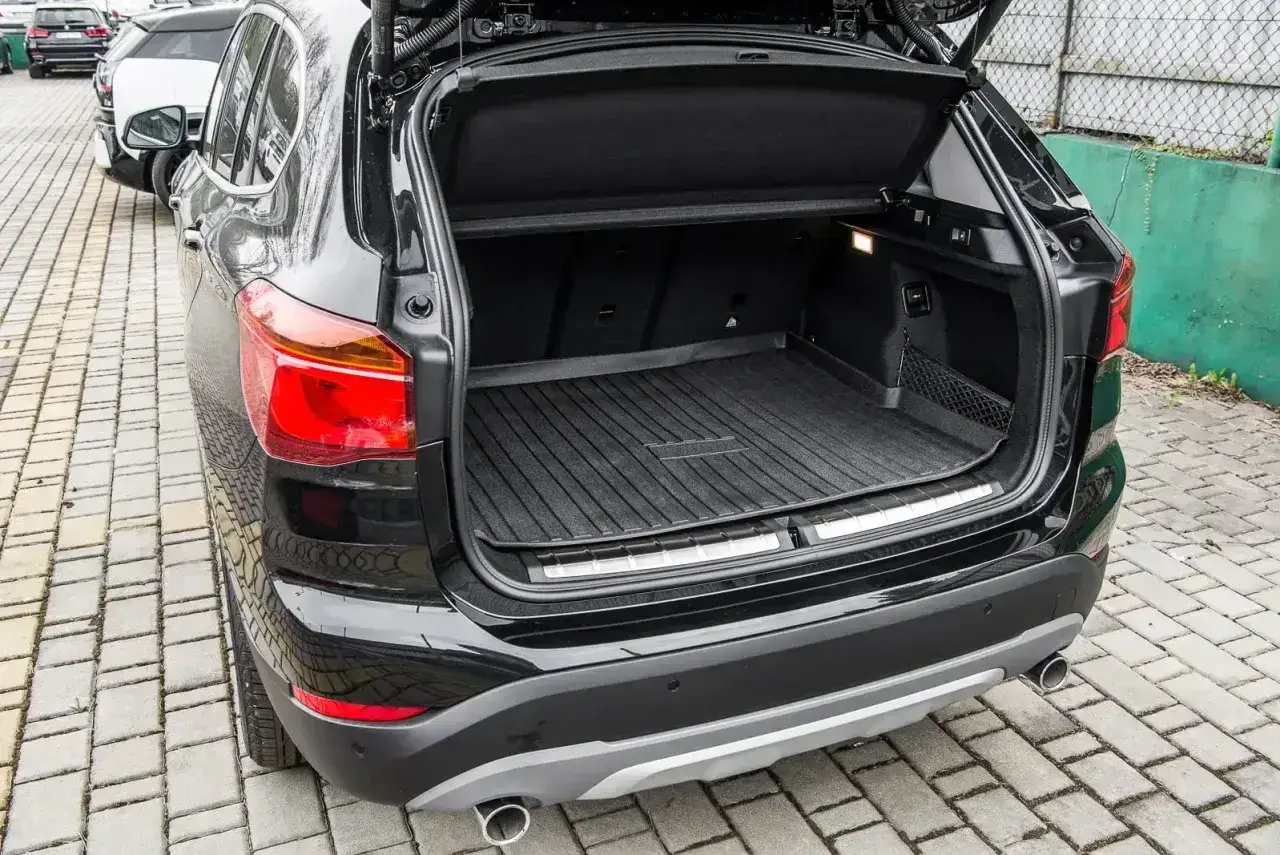 Bagażnik czarnego BMW X1 F48 z gumową matą, gotowy na podróż.