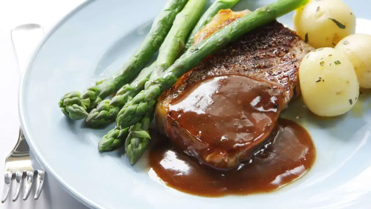 Un steak de bœuf juteux nappé d'une riche sauce roti de boeuf, accompagné d'asperges vertes croquantes et de petites pommes de terre.