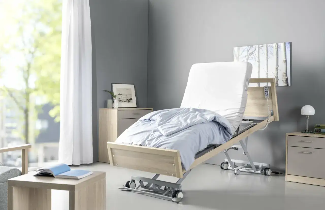 Letto ospedaliero regolabile, parte di una moderna unità di degenza, con lenzuola azzurre e telecomando a portata di mano.