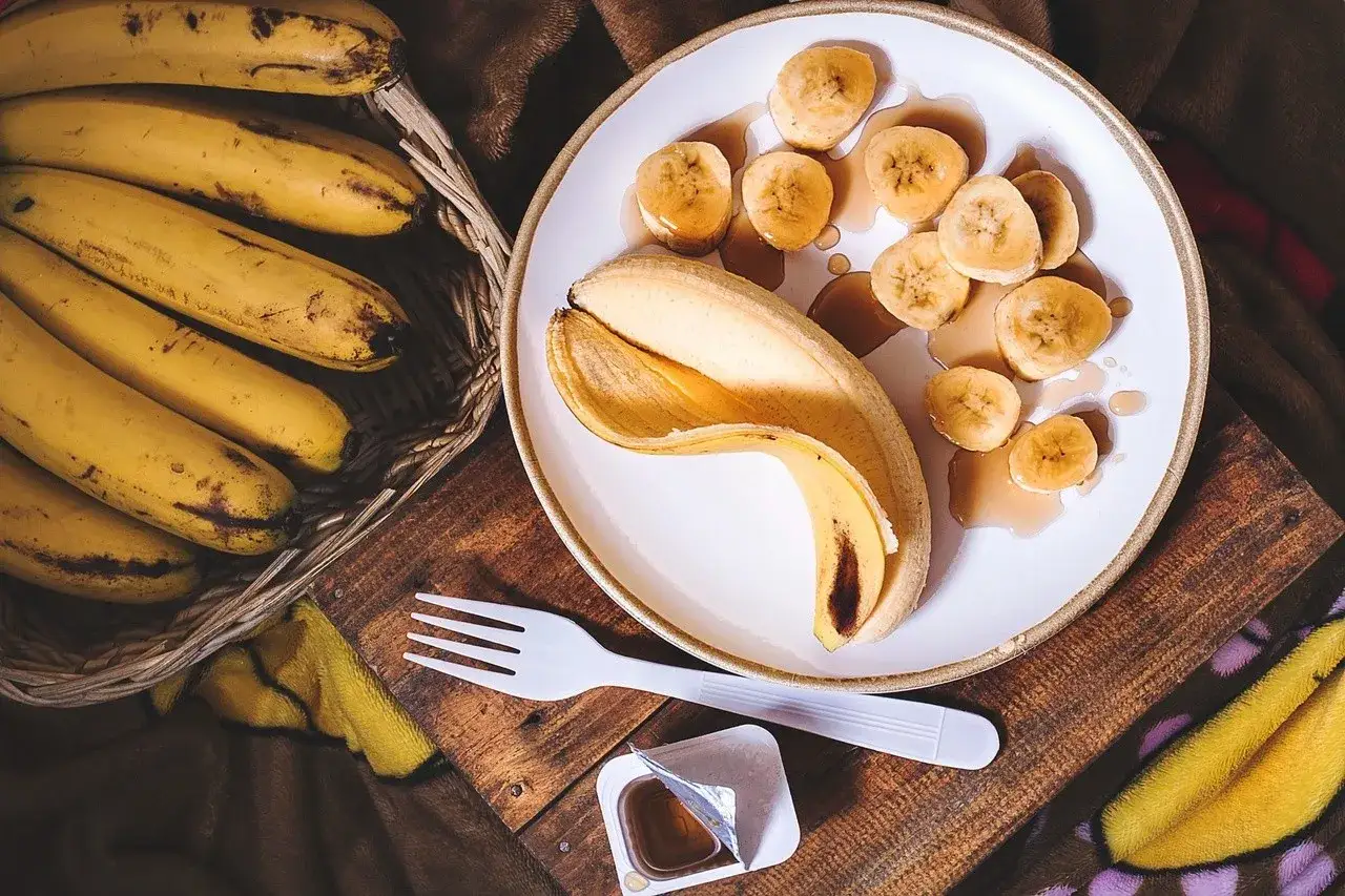 Koszyk pełen dojrzałych bananów obok talerza z pokrojonymi bananami i syropem. Zdrowe banany to świetny dodatek do diety, wspierający pracę nerek.