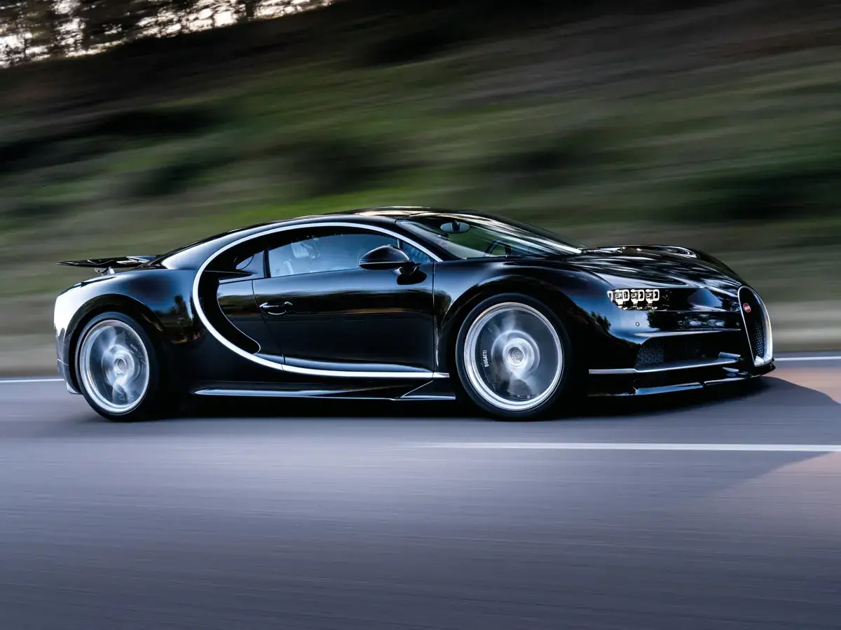Czarne Bugatti Chiron pędzi po drodze. Zastanawiasz się, ile kosztuje Bugatti Veyron? Ten model jest jego następcą.