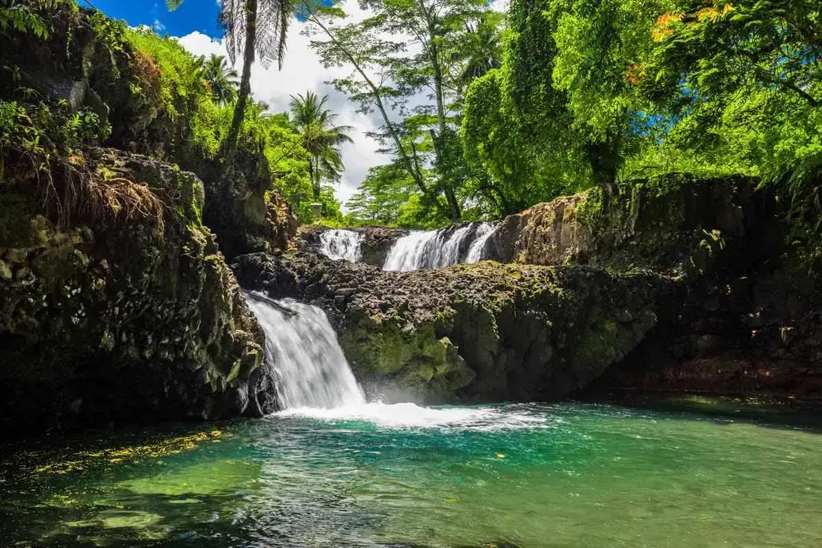 Wodospady na wyspach Samoa, otoczone bujną zielenią i palmami, wpadają do turkusowej wody.