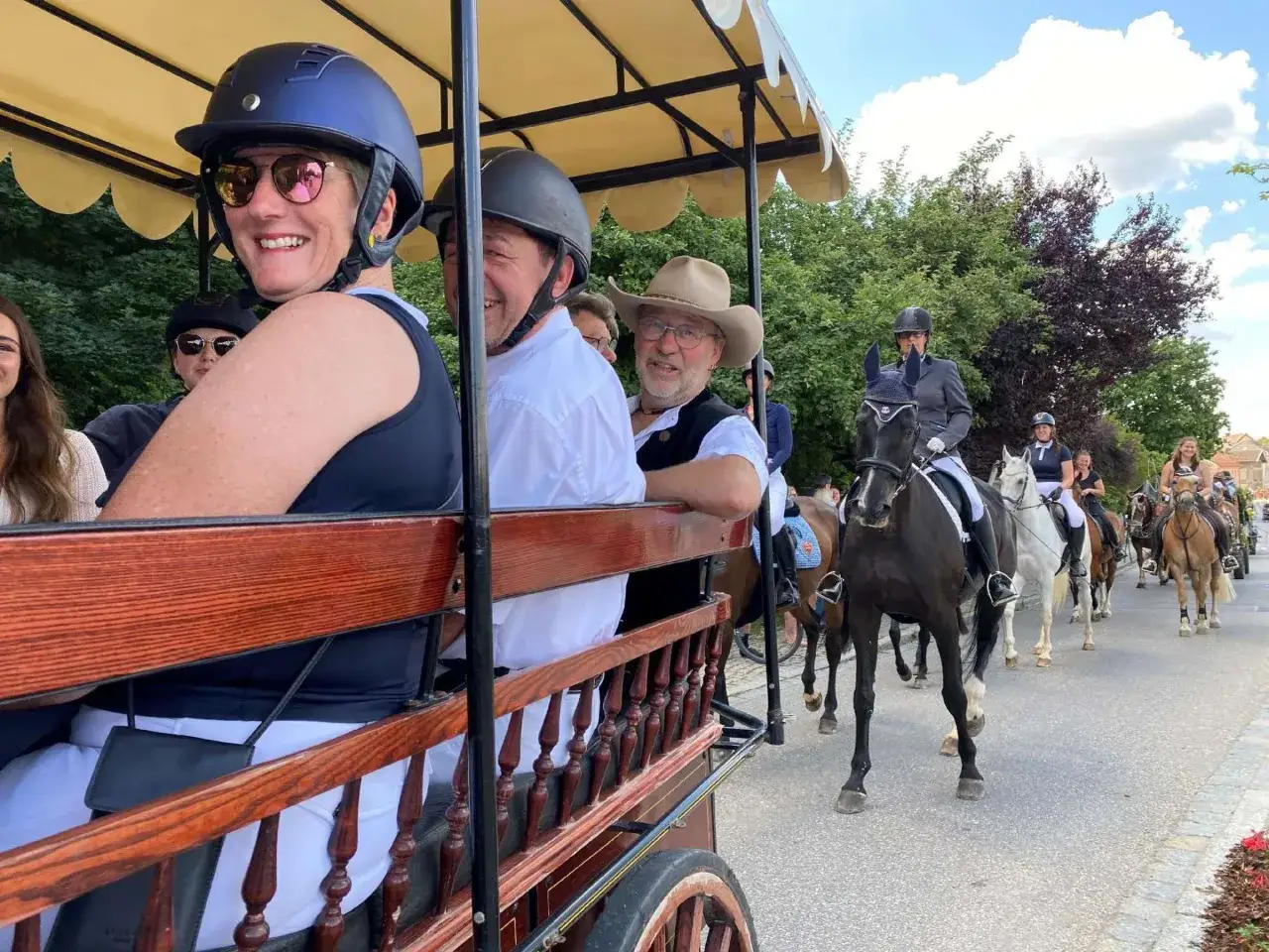 Fr&ouml;hliche Menschen in einer Kutsche und Reiter auf Pferden beim Taufkirchen Volksfest.