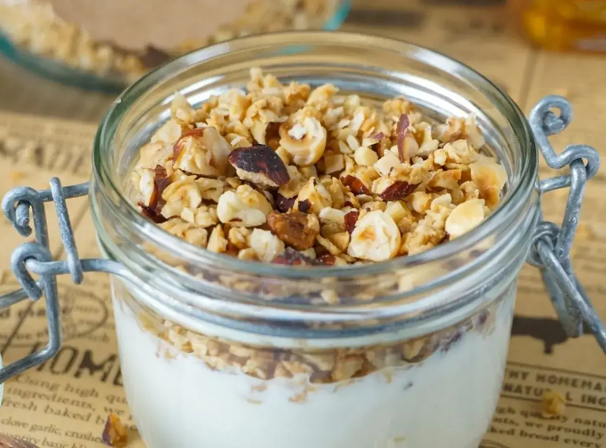 Ein Glas mit Joghurt und selbstgemachtem Granola, das mit Nüssen verfeinert ist. Perfekt für ein gesundes Frühstück.