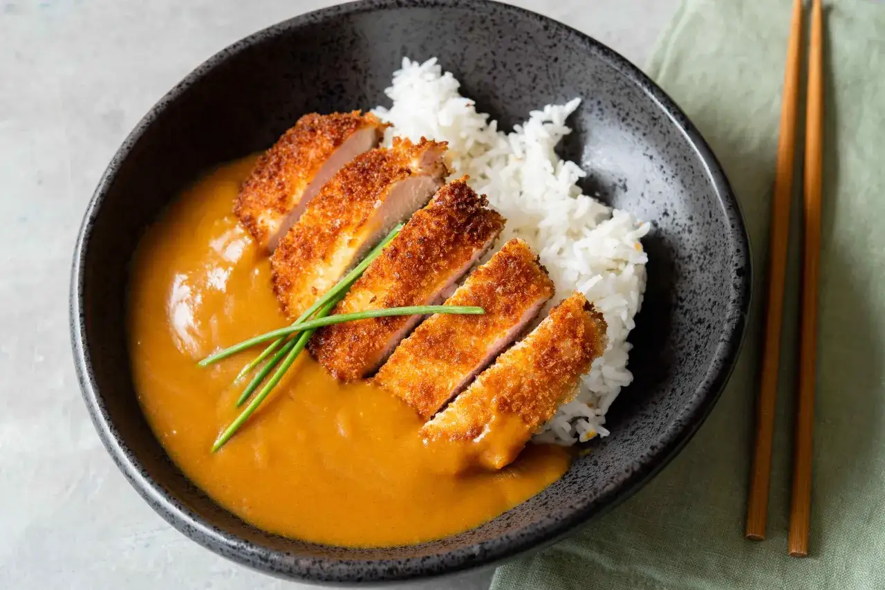 En sk&aring;l med katsu curry, ris och krispigt panerat k&ouml;tt, garnerat med gr&auml;sl&ouml;k. En l&auml;cker japansk r&auml;tt.