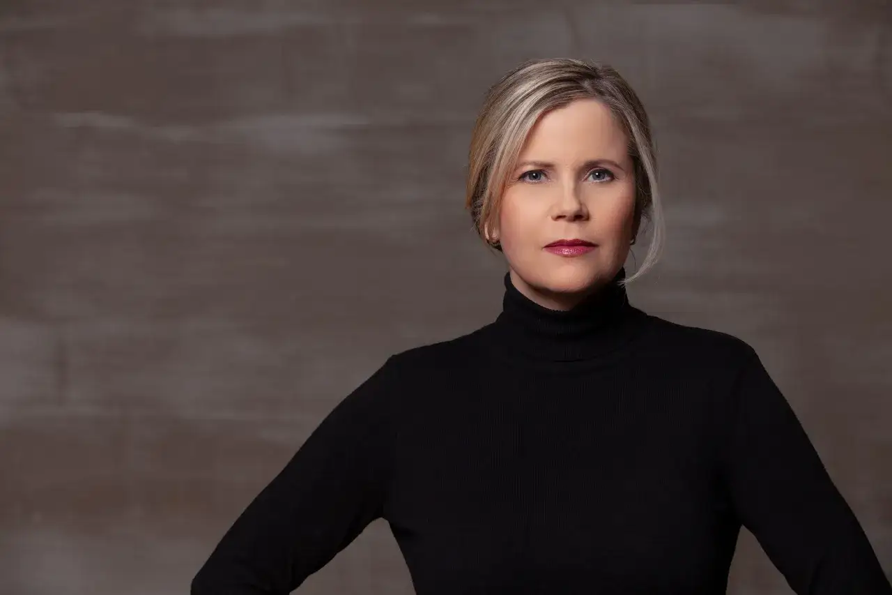 Porträt einer Frau mit blonden Haaren und einem schwarzen Rollkragenpullover. Sie könnte eine Schauspielerin sein, die in **Filme von Michaela Schaffrath** mitspielt.