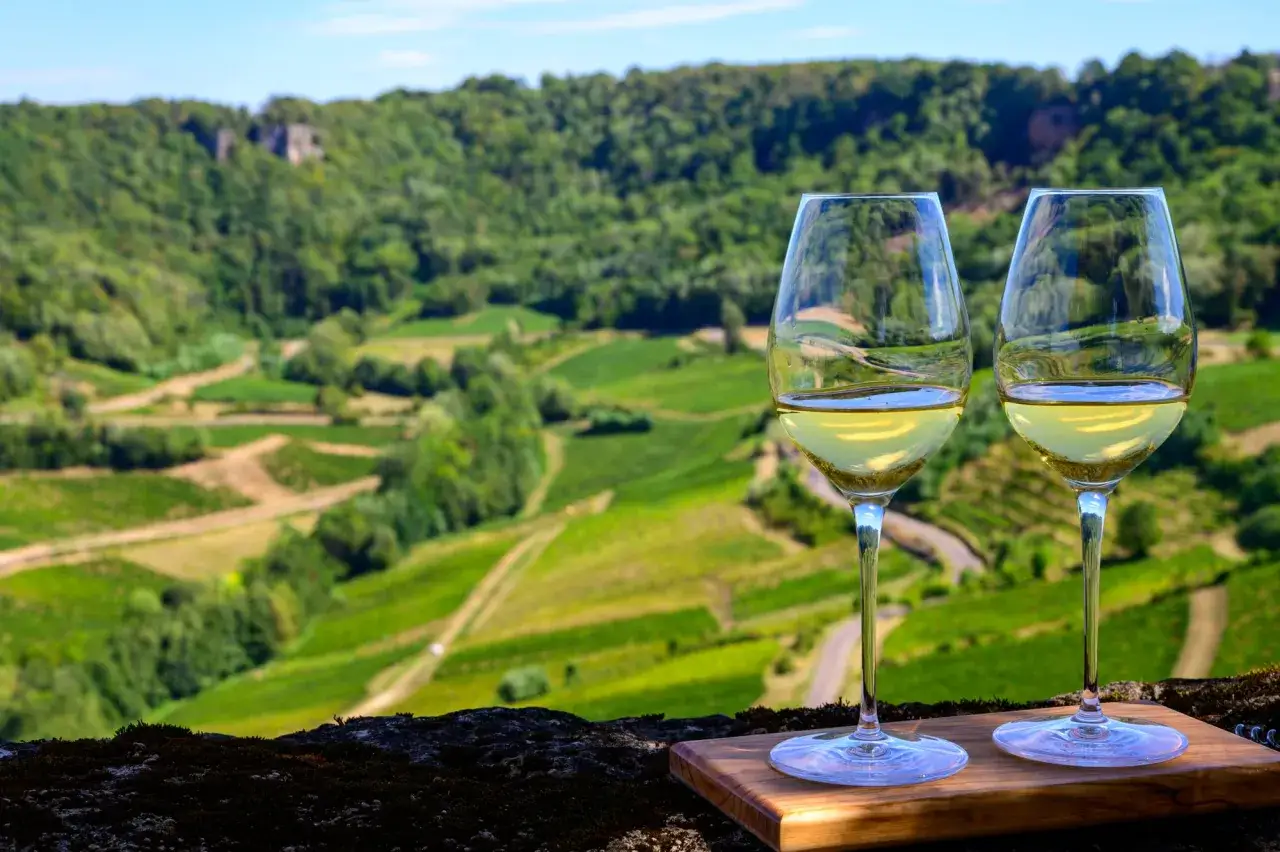 Due calici di vino bianco brillano con vista su vigneti terrazzati. Un assaggio del **Jura vino** in un paesaggio mozzafiato.