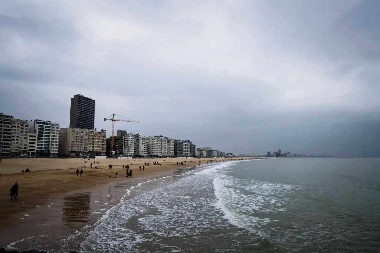 Plaża nad Morzem Północnym, gdzie widać, że Belgia ma dostęp do morza. W tle zabudowania i ludzie spacerujący po piasku.