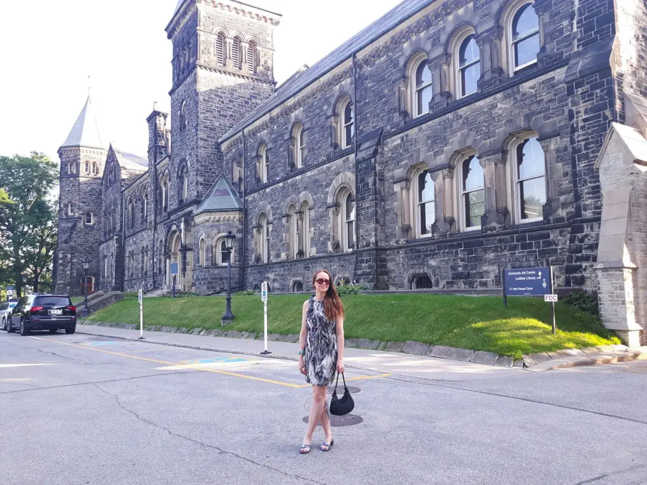 Une femme pose devant l'architecture imposante de l'université de Toronto, un jour ensoleillé.