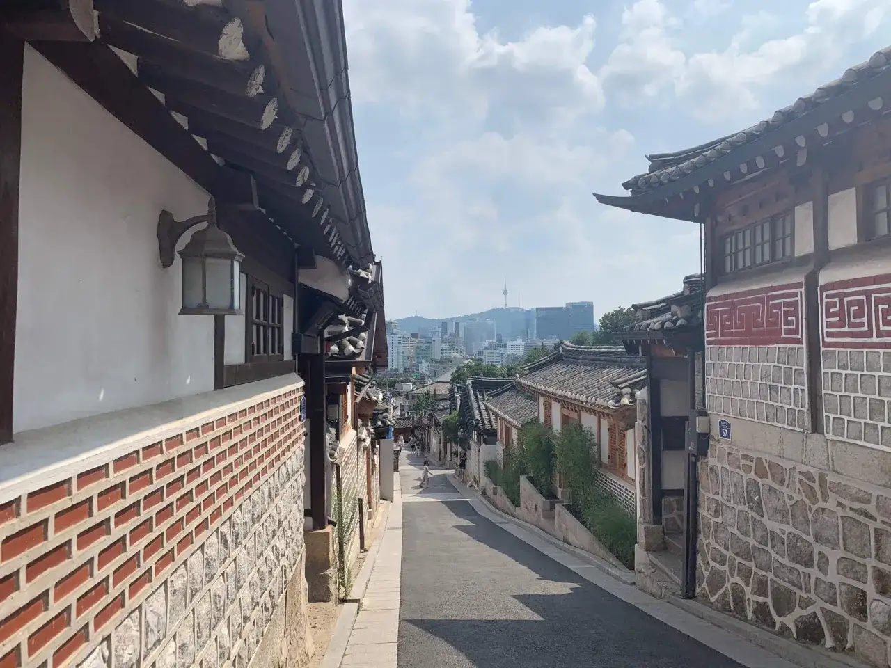 Ulica Bukchon Hanok Village w Seulu, z tradycyjnymi domami i nowoczesną panoramą w tle. Zastanawiasz się, ile kosztuje wycieczka do Seulu?