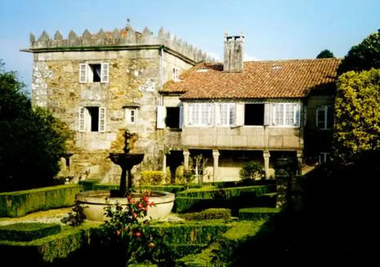 Jardín con fuente y setos cuidados frente a las Torres do Allo, una edificación histórica de piedra con tejado de tejas.