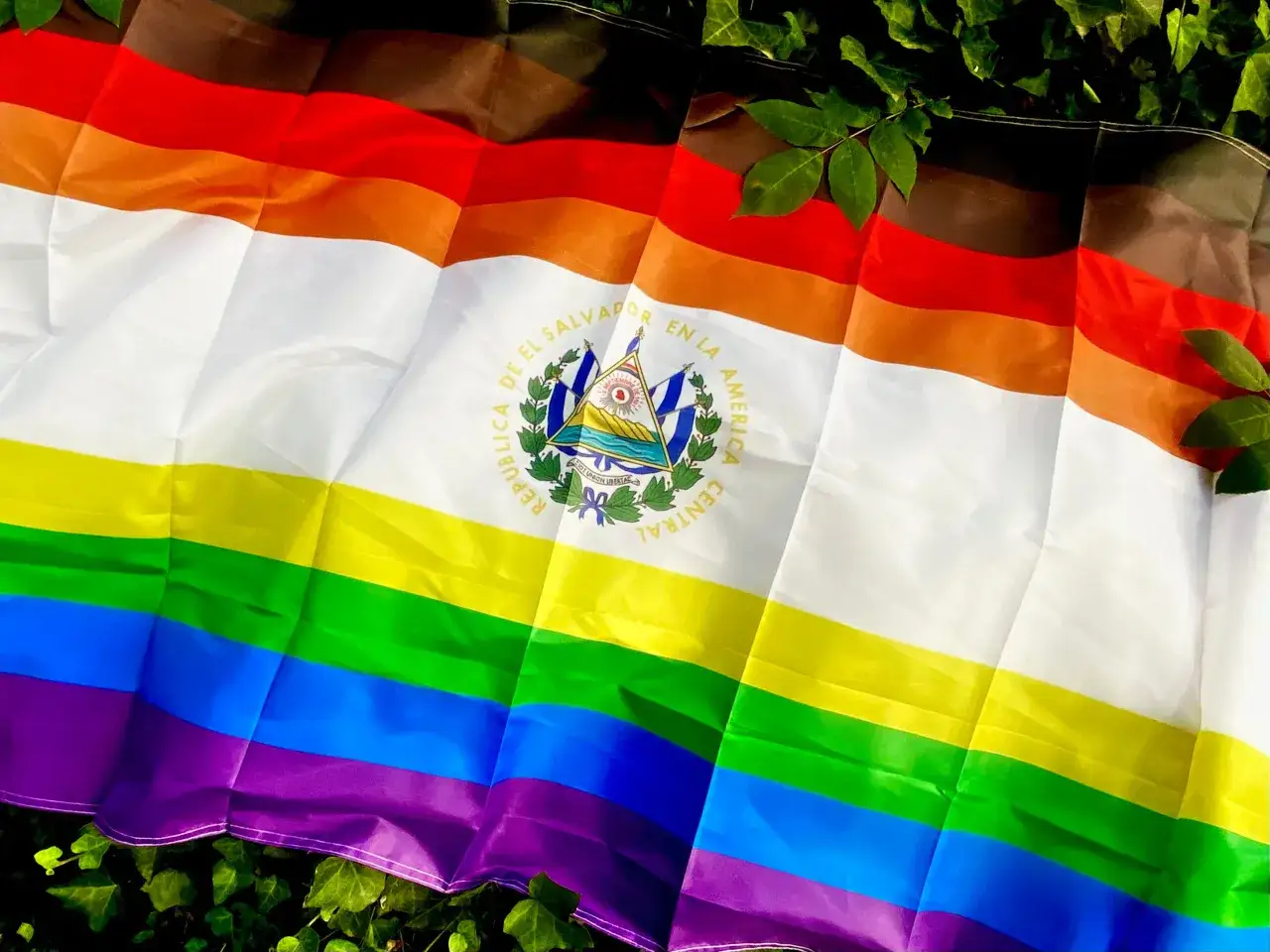 A flag with rainbow and progress pride colors, featuring the El Salvador coat of arms. A symbol of gay pride and identity in El Salvador.