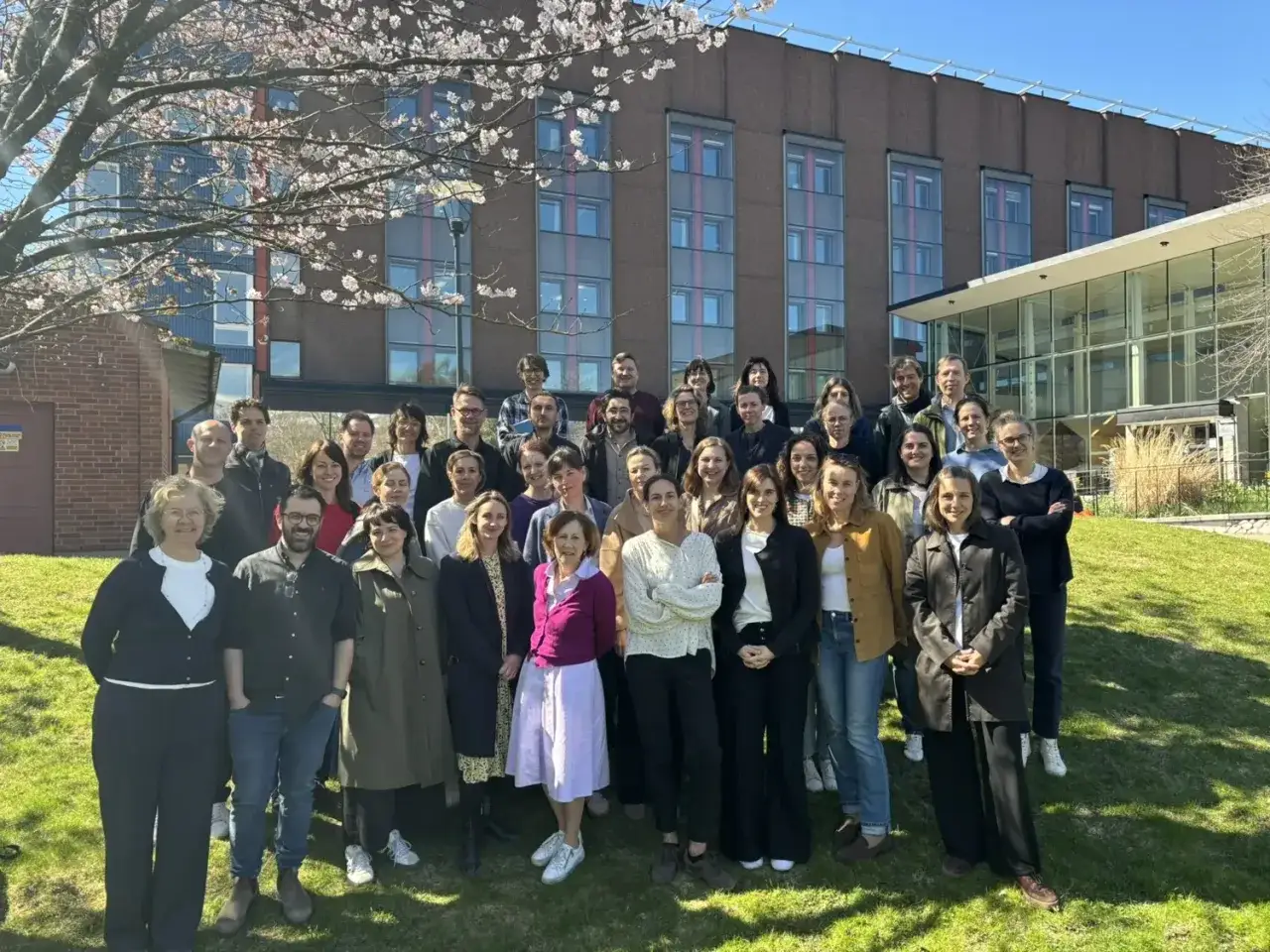 En grupp människor poserar framför en byggnad under en körsbärsblomstrande träd. Kanske en del av en gratis ledarskapsutbildning?