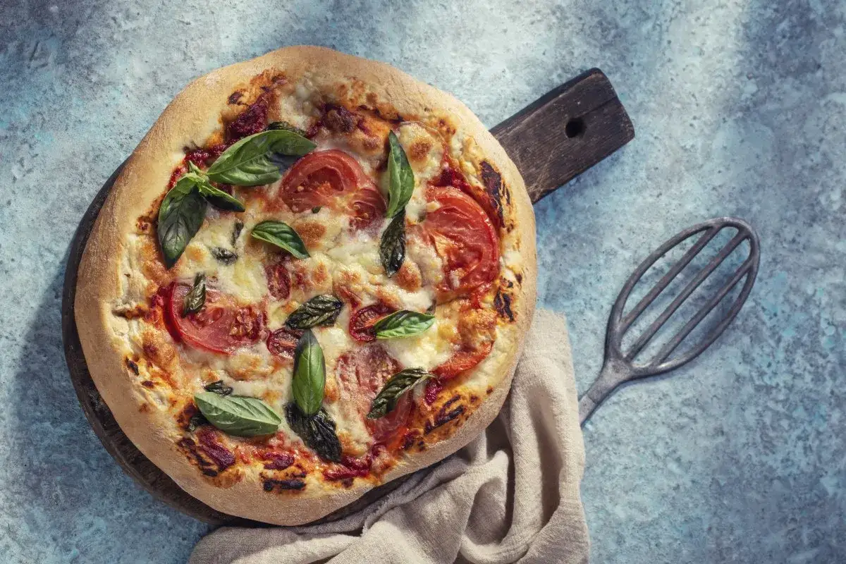Domowa pizza na proszku do pieczenia, z pomidorami i bazylią, wygląda apetycznie na drewnianej desce.