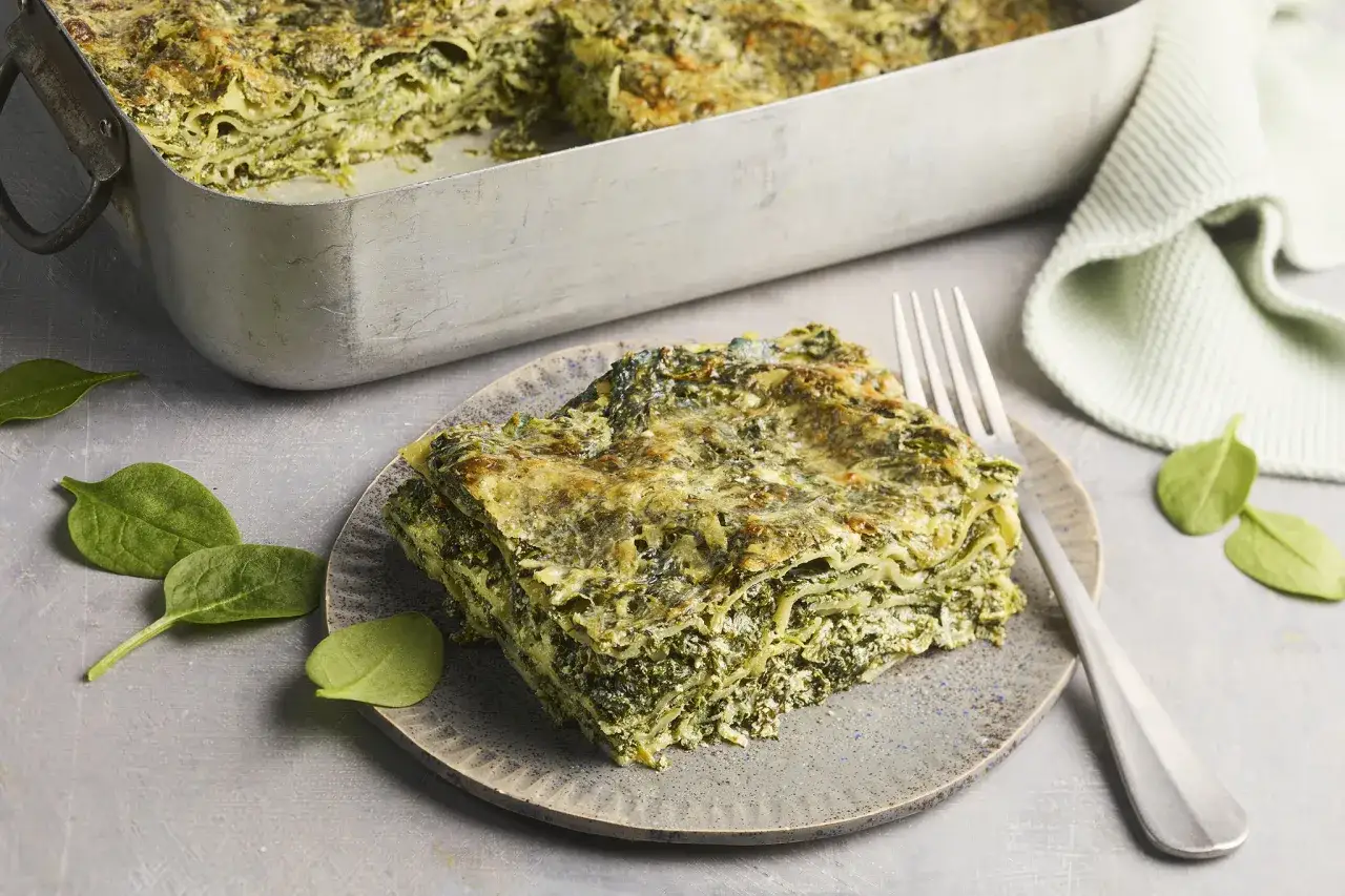 Herzhaftes Spinatlasagne Rezept: Eine Portion der cremigen Lasagne mit viel Spinat und K&auml;se auf einem Teller, daneben frische Spinatbl&auml;tter.