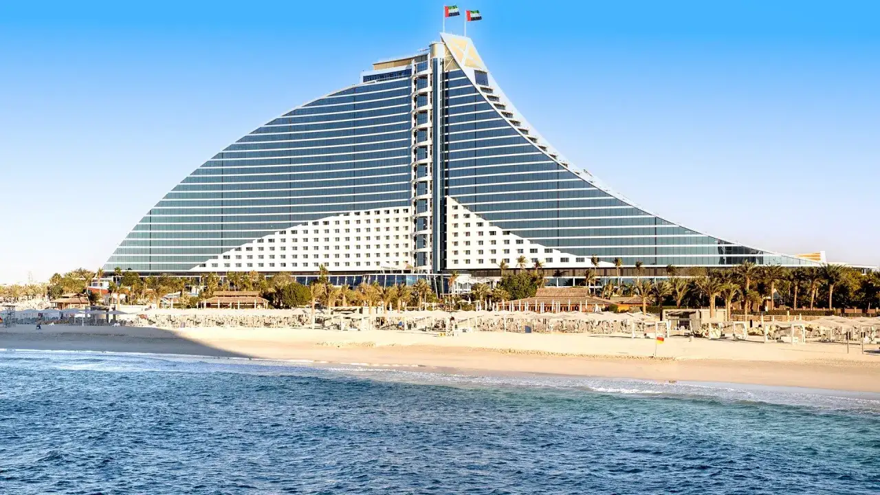 Luksusowe wakacje w Dubaju: hotel w kształcie żagla nad Zatoką Perską, z piaszczystą plażą i palmami.