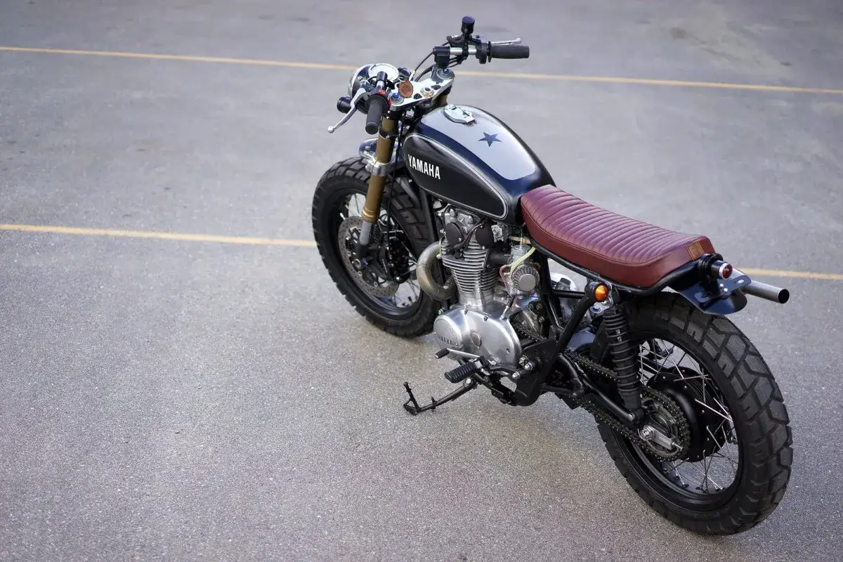 Klasyczny motocykl Yamaha z brązowym siedzeniem i czarnym bakiem, gotowy do podr&oacute;ży. Yamaha, kraj pochodzenia, to symbol jakości.