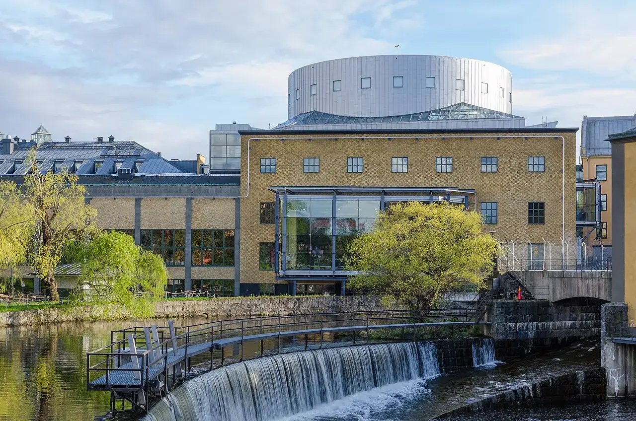 Louis de Geer Konsert & Kongress med en forsande vattenfall framför. En modern byggnad med en rundad takdel.