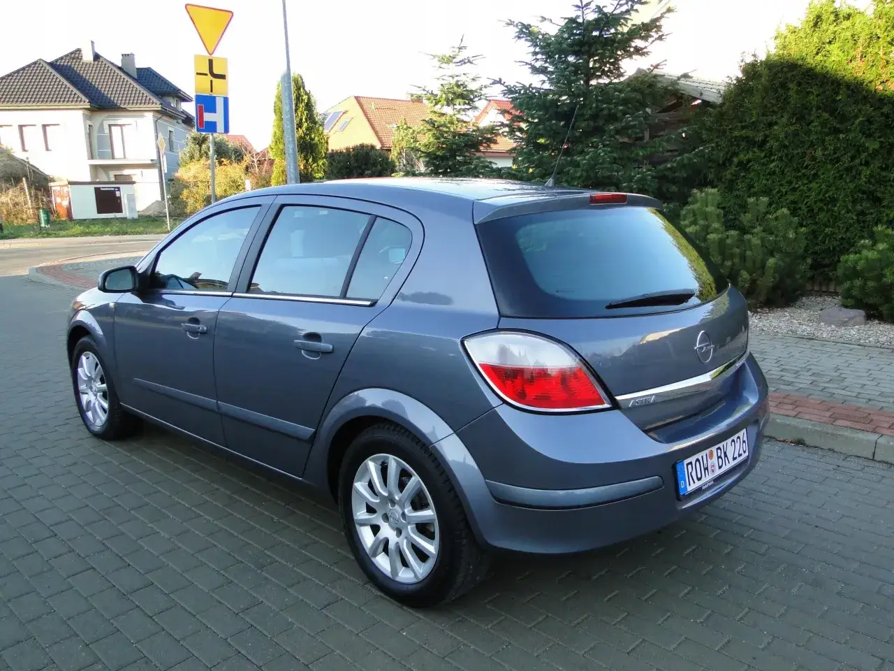 Szary Opel Astra H 1.6 benzyna stoi na kostce brukowej przed domem.