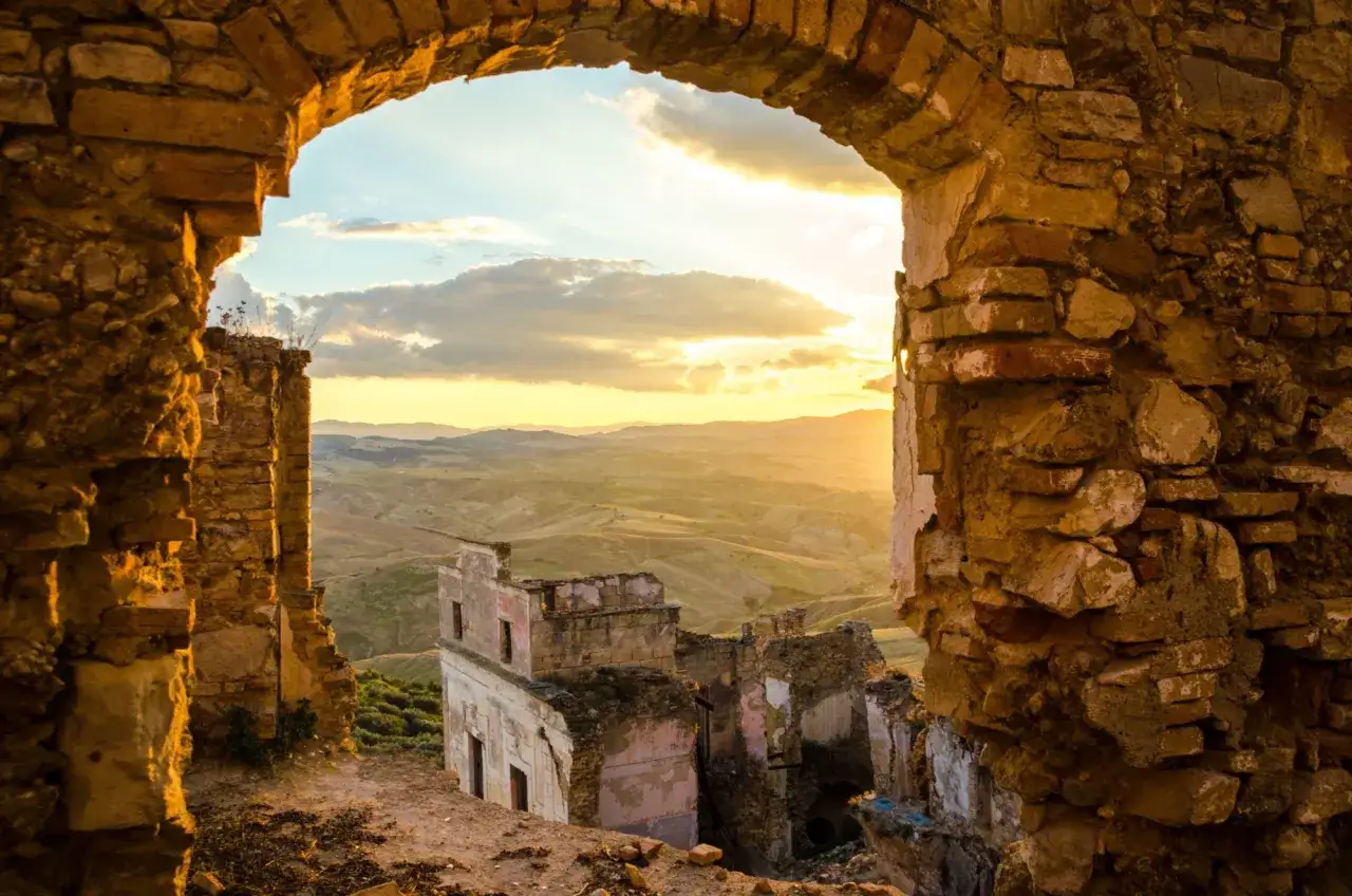 Rovine di **paesi abbandonati in Italia** illuminate dal tramonto, con un paesaggio collinare sullo sfondo.