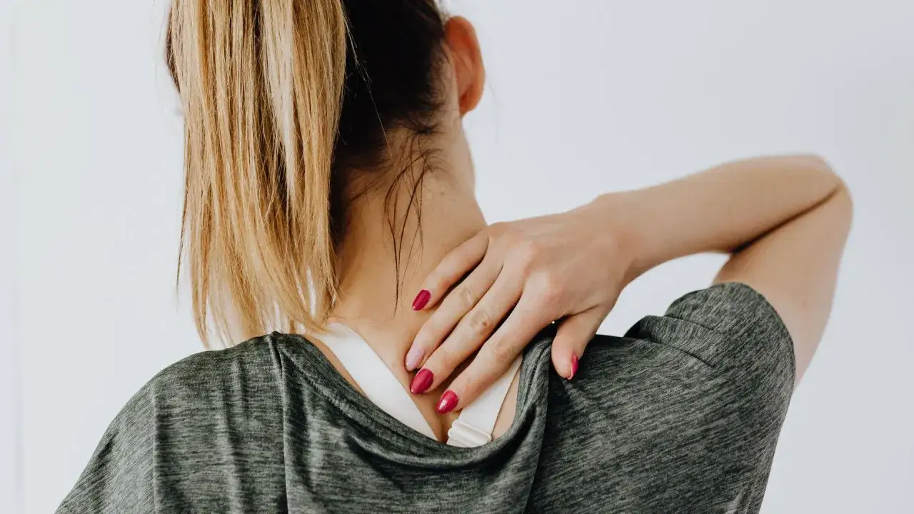 Une femme se tient le cou, souffrant de douleurs articulaires. La vitamine B12 pourrait aider à soulager ces maux.