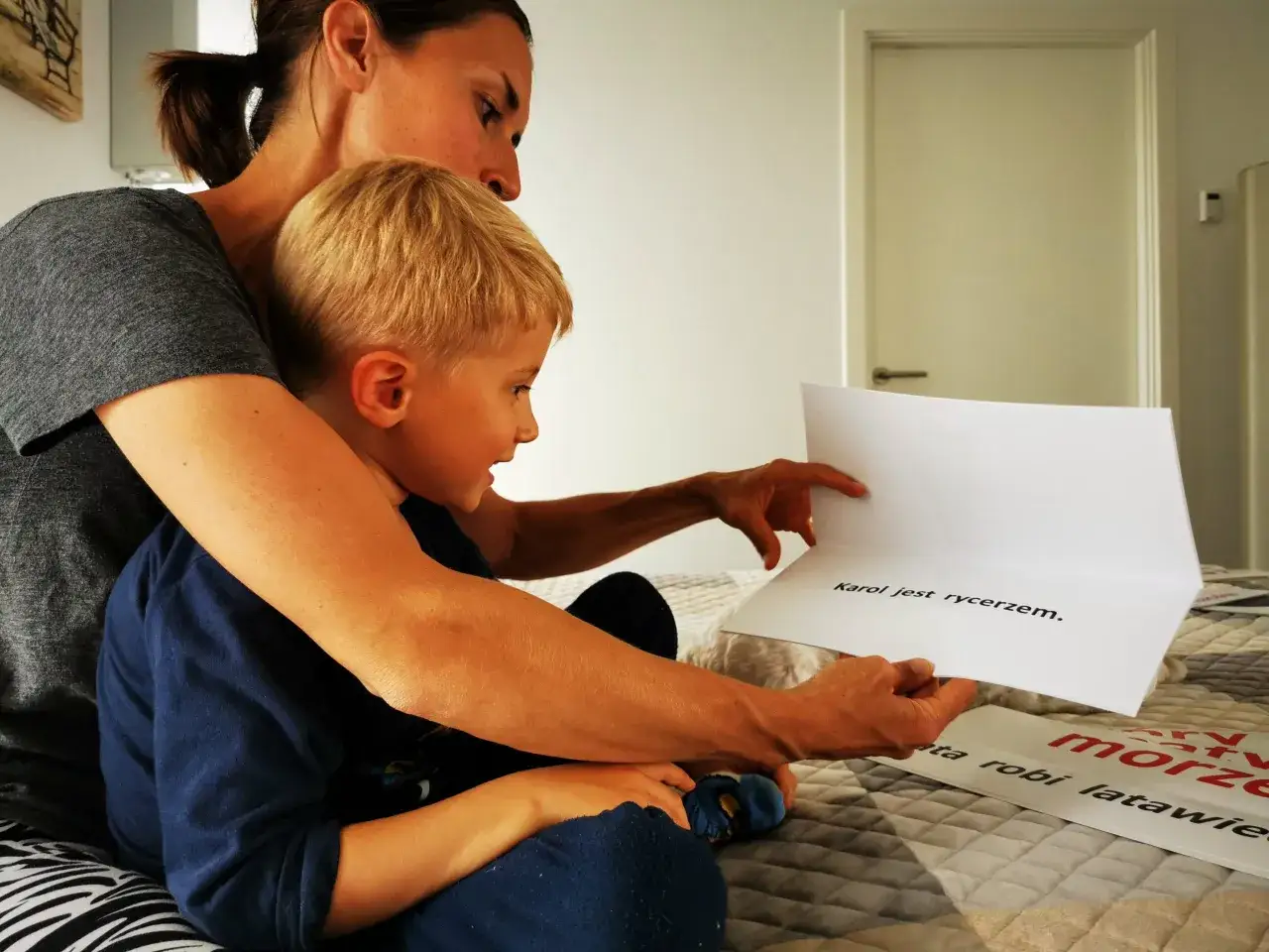 Mama z synem czytają książkę, ćwicząc podział na głoski. Na kartce napis: