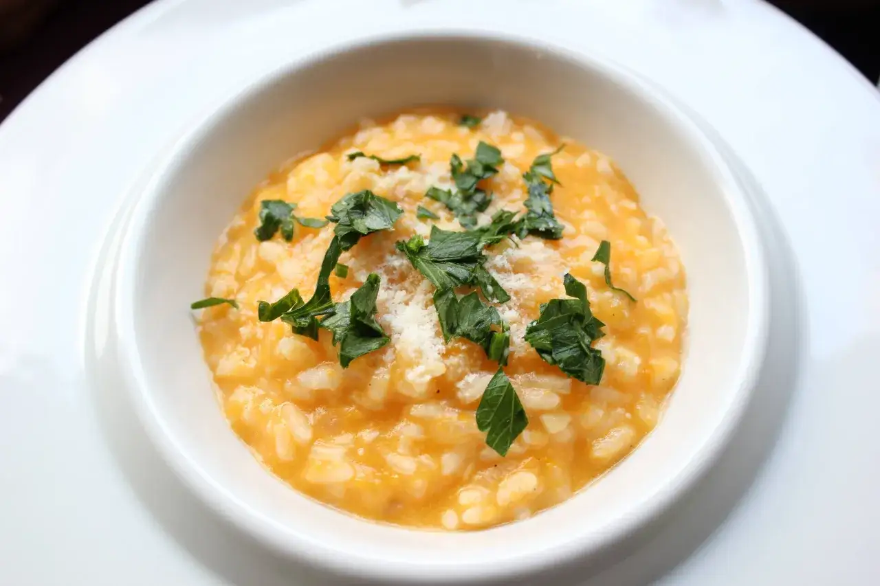 Cremoso risotto de calabaza, adornado con perejil fresco y queso rallado, servido en un plato blanco.