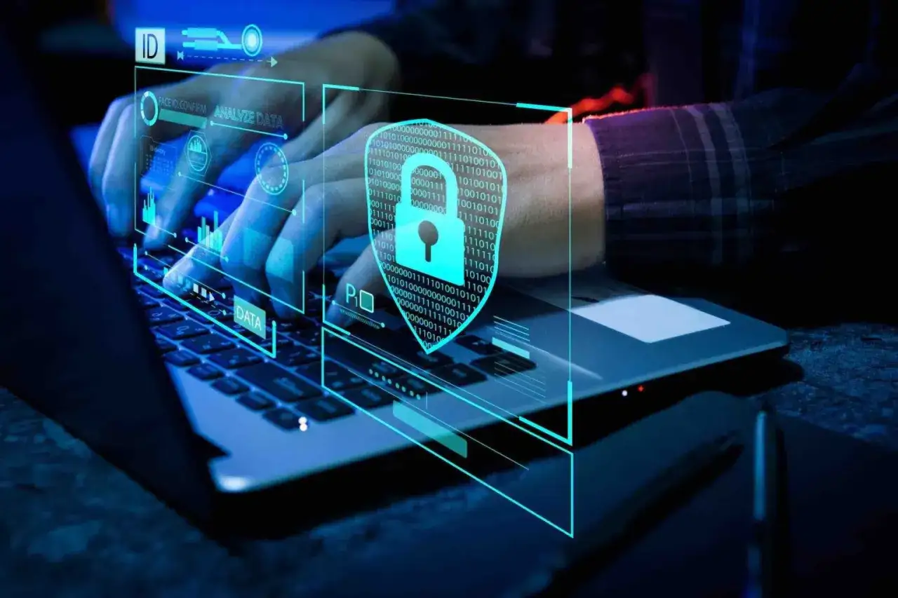 Manos tecleando en un portátil con interfaz futurista de seguridad y datos. El escudo con candado simboliza la protección, el no repudio significado en la seguridad digital.
